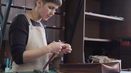 Leather manufacture workshop. Young female tailor works on leather handcrafted bag. Leather craftsman working in workshop studio