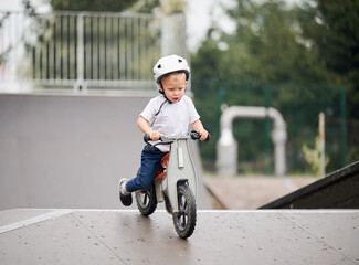 Child riding balance bike. Male toddler kid in helmet learning to ride on run bicycle at skate park.