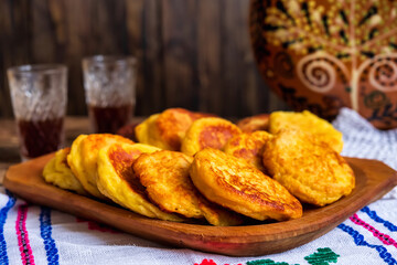 Traditional Romanian and Ukranian cheese pancakes cooked in local rustic style on a traditionally decorated tablecloth and two glasses with local drink
