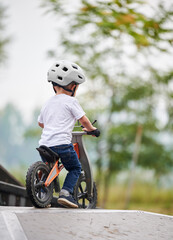 Back view child riding balance bike. Male toddler kid in helmet learning to ride on run bicycle at...