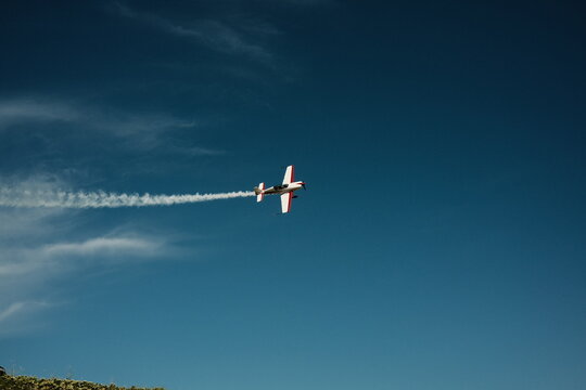  A small plane maneuvers in a blue sky with a contrail. High quality photo