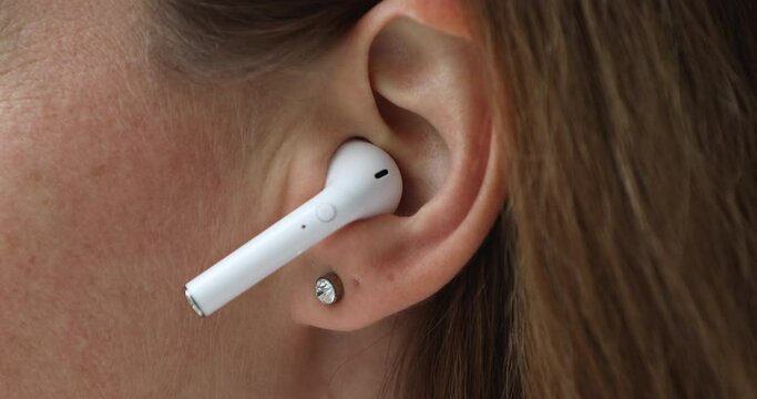Close up cropped view unknown female put on white modern wireless earphone in ear, hear music, play favourite song, listen audio voice message, start work out with popular track. Technology concept