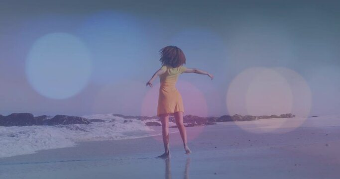 Animation of light spots over african american woman dancing on beach