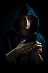 Portrait of a young hooded man who is using a smartphone