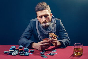 A wealthy mature man drinking brandy and playing poker with the excitement in a casino.