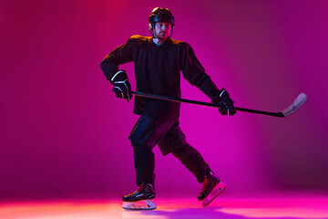 Man, professional hockey player training in special uniform with helmet isolated over pink background in neon. Winning match