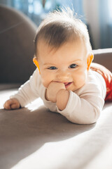 Baby girl lying on comfort bed, suck fingers, looking at camera. Body care. Smiling happy child....