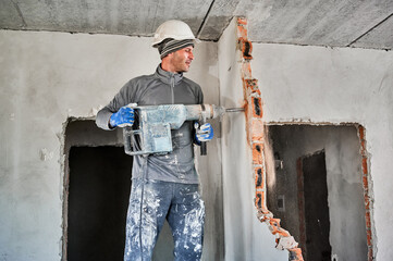 Side view of man builder in workwear drilling wall with hammer drill. Male worker using drill...