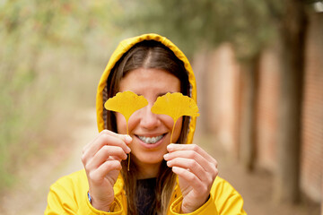 Selective focus of unrecognizable woman holding yellow tree leaves. Horizontal cropped view of woman hiding eyes behind yellow autumn leaves outdoors. Nature and people backgrounds.