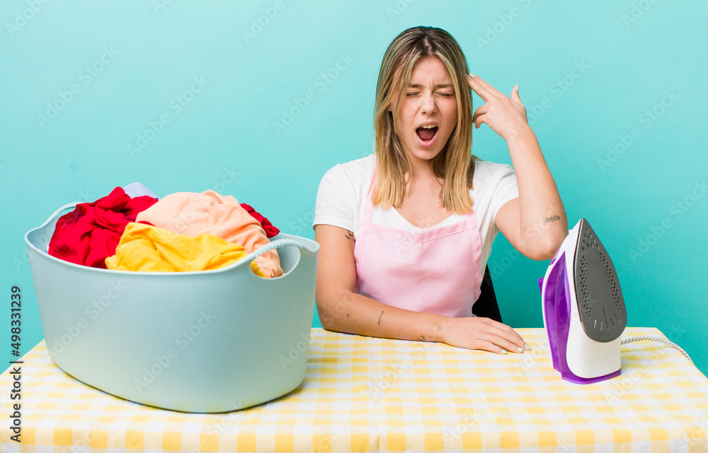 Wall mural pretty blonde woman looking unhappy and stressed, suicide gesture making gun sign. iron and clothes 