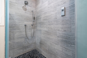 Walk-in shower with smooth gray tile walls and pebble rock flooring.