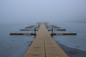 pier on frozen lake with fog background