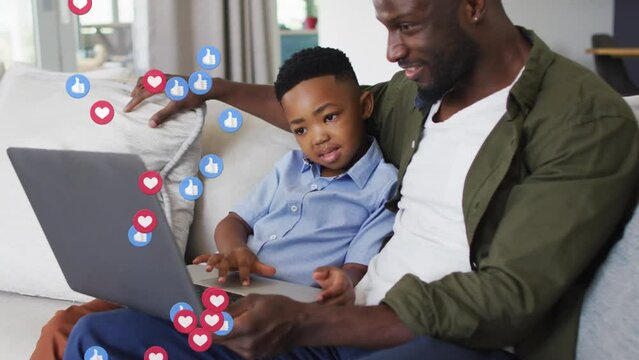 Animation of emoticons over happy african american father and son using laptop