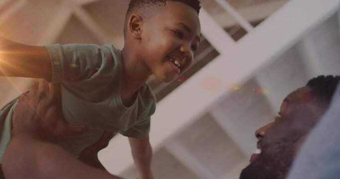 Animation of lights over happy african american father and son having fun at home
