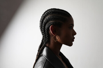 Side portrait of African young woman with braids posing on white wall.  - obrazy, fototapety, plakaty