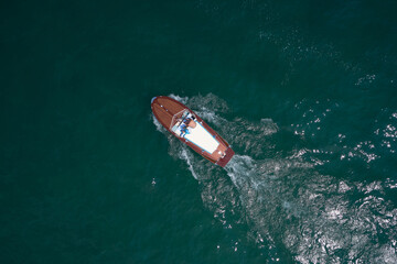 Fototapeta premium People on an Italian wooden boat, top view. Old boat on Lake, Italy. Classic wooden boat in motion drone view.