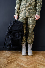Fototapeta na wymiar cropped view of military woman with black backpack near dark wall.
