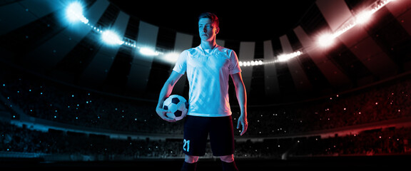 One professional soccer, football player in football kit standing with ball over dark night stadium...