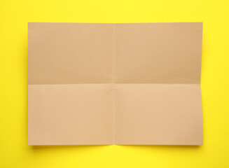Sheet of brown paper on yellow background, top view