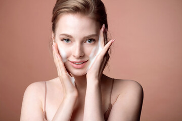 Smiling young blond woman washing foam face by natural foamy gel. Satisfied girl with bare...
