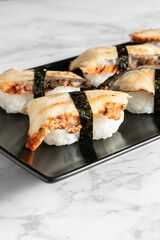 Sushi nigiris with eel fish rolled with a strip of seaweed served on a black plate on a marble table. Delicious traditional Japanese food, tasty seafood, restaurant concept, food background. Vertical