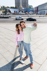 Positive couple gesturing and taking selfie on urban street.