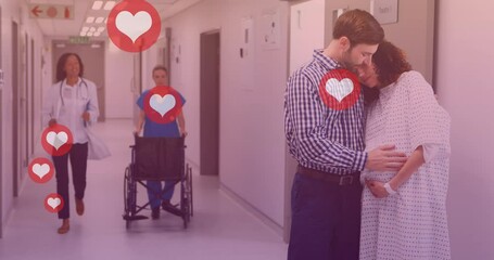 Animation of heart icons over caucasian man embracing pregnant wife in hospital