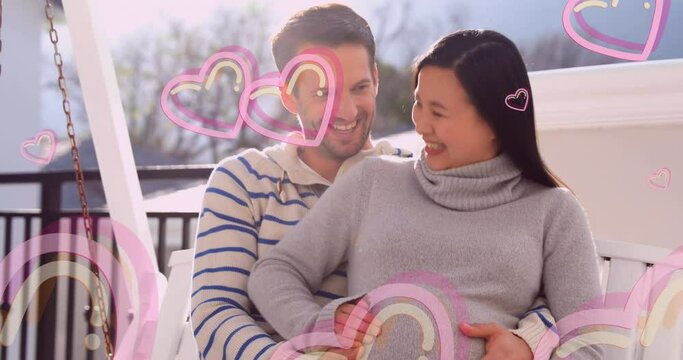 Animation of heart icons over happy caucasian man embracing pregnant wife