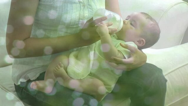 Animation of light spots over biracial mother feeding her baby