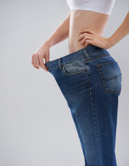 You can achieve this too. Cropped shot of a woman showing off her weightloss with a large pair of trousers.
