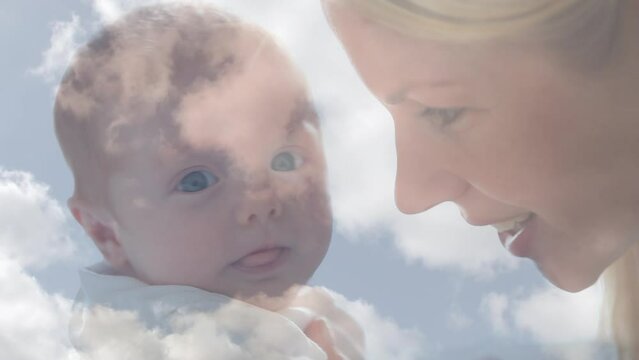 Animation of clouds over happy caucasian mother kissing her baby