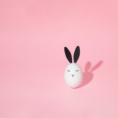 White easter egg with bunny face and eyes on bright pink background with shadow.