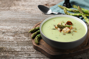 Bowl of delicious asparagus soup on wooden table, space for text
