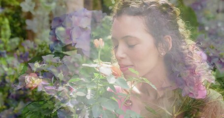 Animation of glowing lights over happy biracial woman smelling flowers in garden
