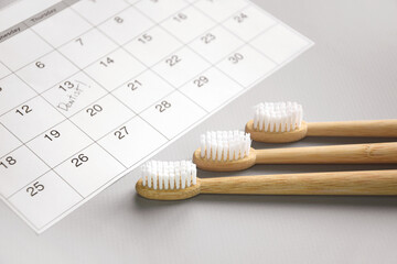 On a light gray background, there is a calendar with a dentist's note and toothbrushes.