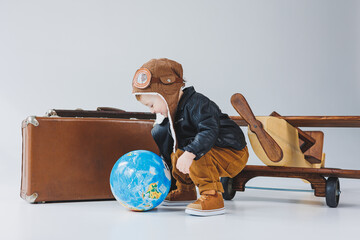 A boy in a leather jacket and a pilot's hat, a wooden plane, a globe, brown suitcases. Children's...