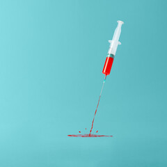 Creative concept of vaccination on a blue background. Medical syringe spewing red liquid with...