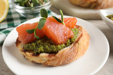 Delicious bruschetta with salmon and pesto sauce on table, closeup