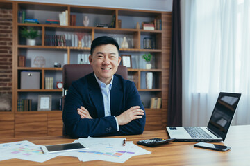 Asian man, businessman, boss in a suit, sitting in a chair at a table in the office, working with a...