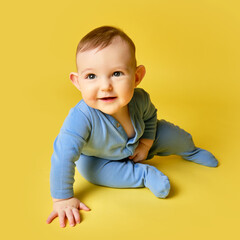 Naklejka premium Happy toddler baby sits on studio yellow background. Funny child boy at the age of six months with a smile on his face, copy space