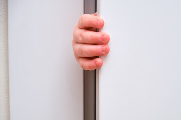 Toddler baby boy holds the edge of the open door with his hand. Close-up child hand at the door jamb