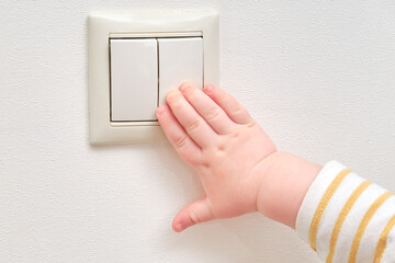 Toddler baby boy turns the light on and off with an electric switch. Close-up of a child hand at a...