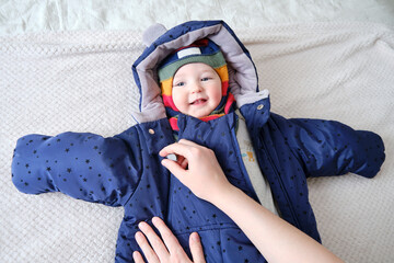 A mother woman puts on a warm jacket for a baby boy. Mom dresses a happy child in winter clothes on...