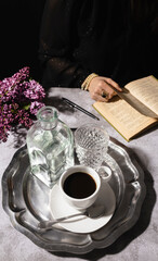 Fototapeta na wymiar Mysterious woman drinking black coffee with glass and jug of water on elegant silver tray with dark background