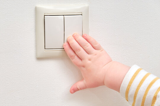 Toddler baby boy turns the light on and off with an electric switch. Close-up of a child hand at a double light switch