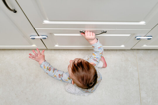 Toddler baby boy rips off a cabinet drawer with his hand. The child holds the cabinet door handle, small kid