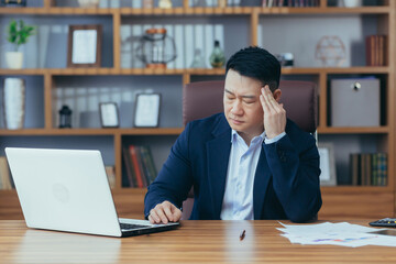 Tired young asian man businessman, worker, lawyer at work. He has a headache, keeps his hands on...