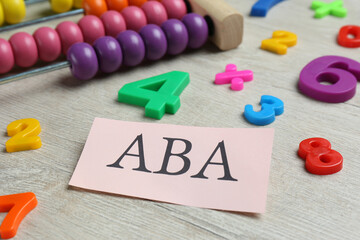 Paper sheet with abbreviation ABA (Applied behavior analysis), abacus and colorful numbers on white wooden table, closeup - obrazy, fototapety, plakaty