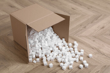 Overturned cardboard box with styrofoam cubes on wooden floor