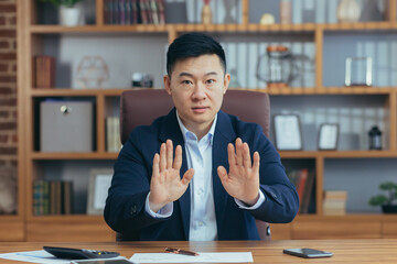 Asian man diplomat, director, businessman looking at the camera smiling, concluding a contract, holding a meeting, video call conference, consults. Explains, sits at a table in the office at work